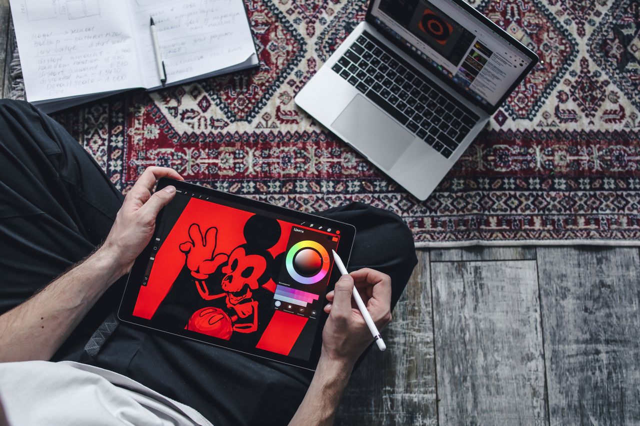 Home A person drawing on a digital tablet while seated on a patterned rug indoors.